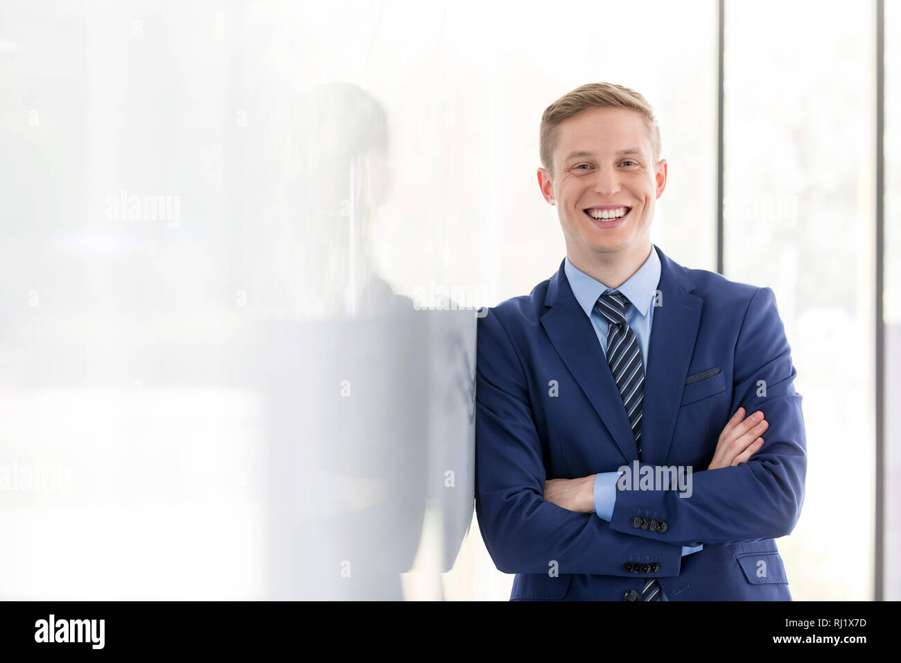 Portrait of smiling young man leaning on wall at office Banque D'Images