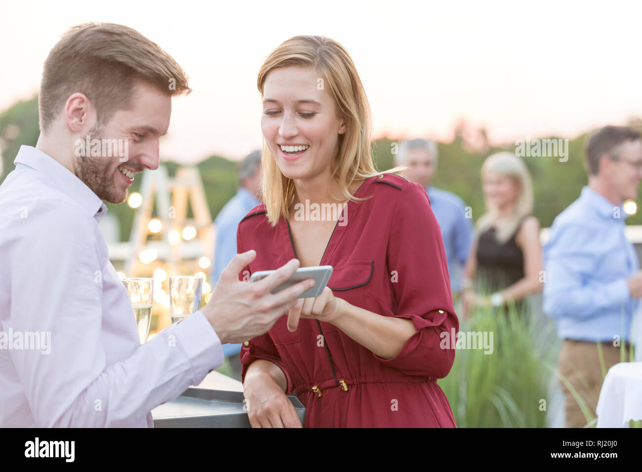 Smiling young woman partager smartphone avec businesswoman pendant party sur le toit Banque D'Images