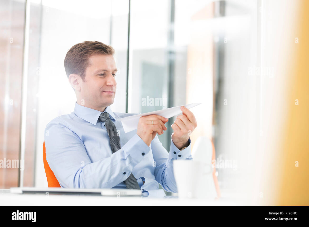 Creative businessman holding paper plane tout en restant assis dans office Banque D'Images