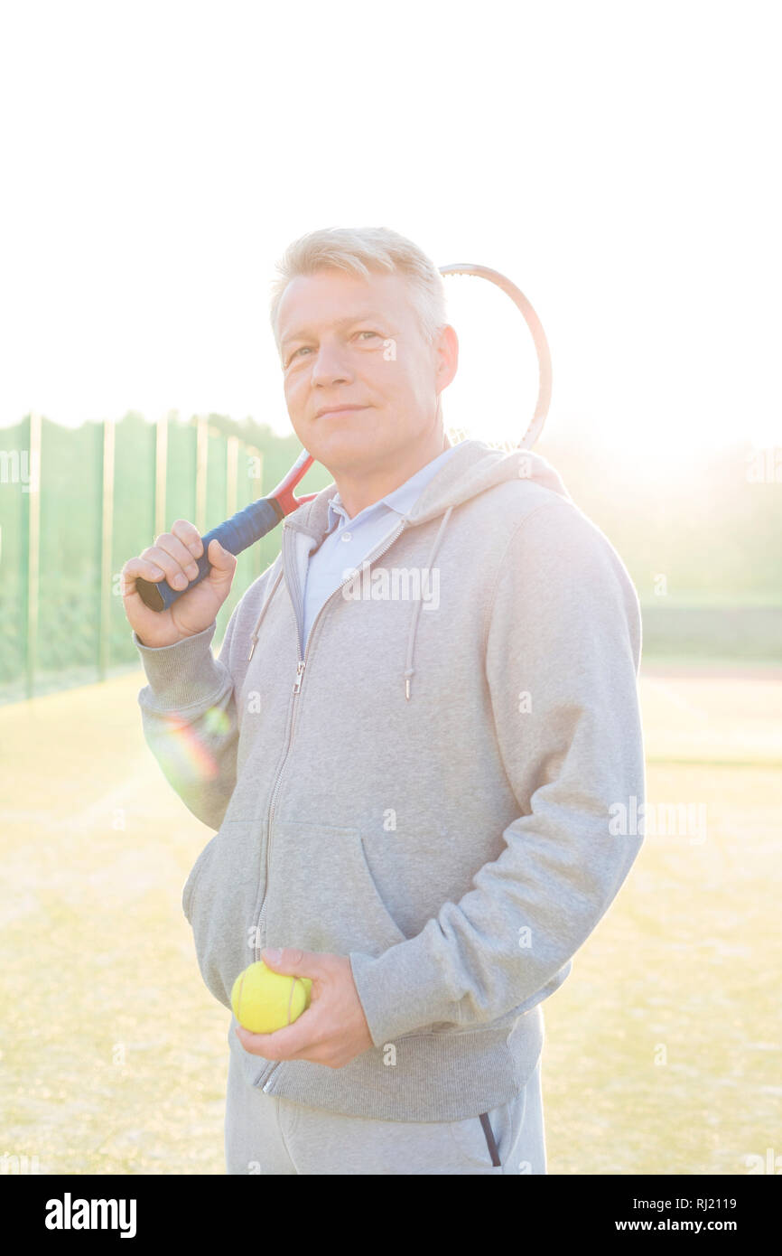 Retour allumé d'homme confiant holding tennis ball et racket sur cour contre un ciel clair Banque D'Images