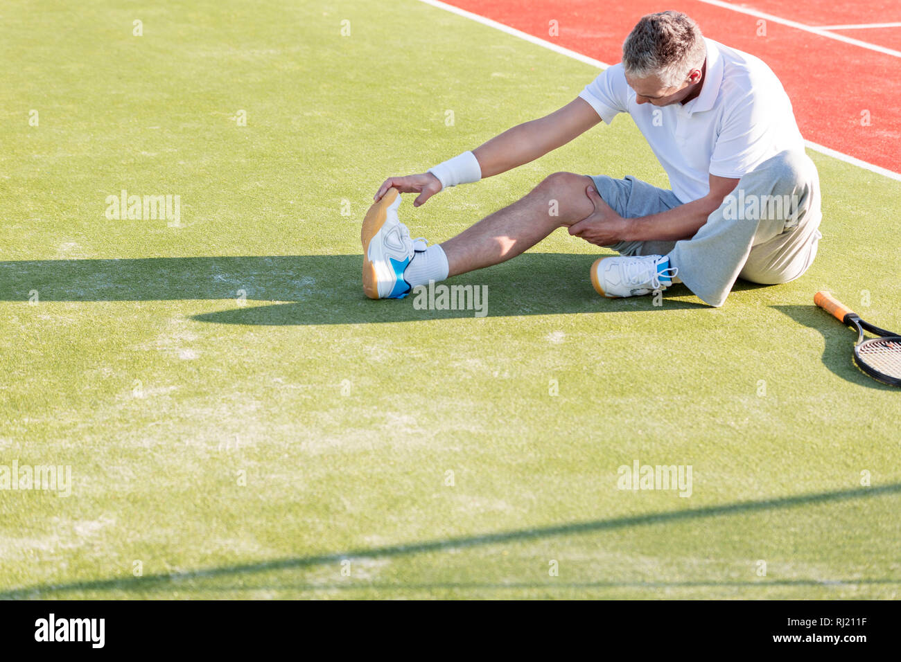 High angle view of mature man réchauffe tout en s'étendant sur un court de tennis Banque D'Images