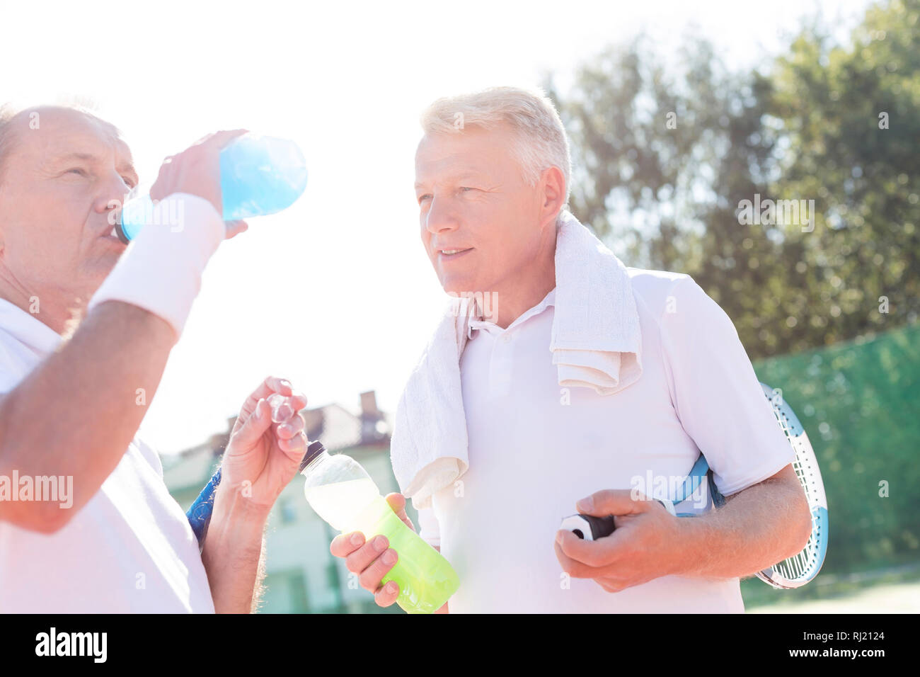 Homme mature à la recherche de la bouteille de boisson ami senior en se tenant sur le court de tennis durant l'été Banque D'Images