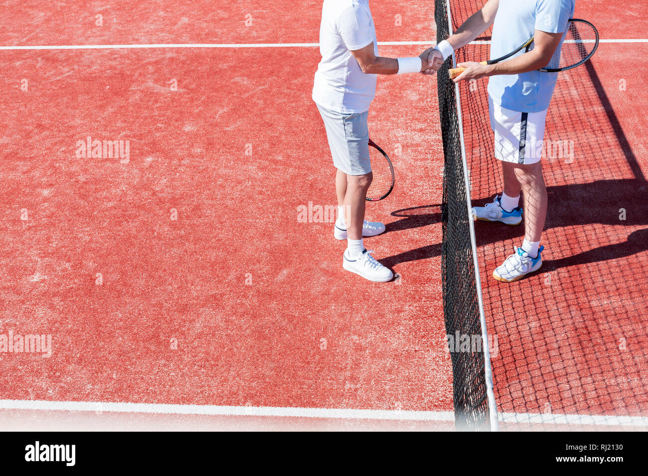 La section basse des hommes se serrer la main en se tenant debout par tennis net sur cour rouge au cours de match Banque D'Images