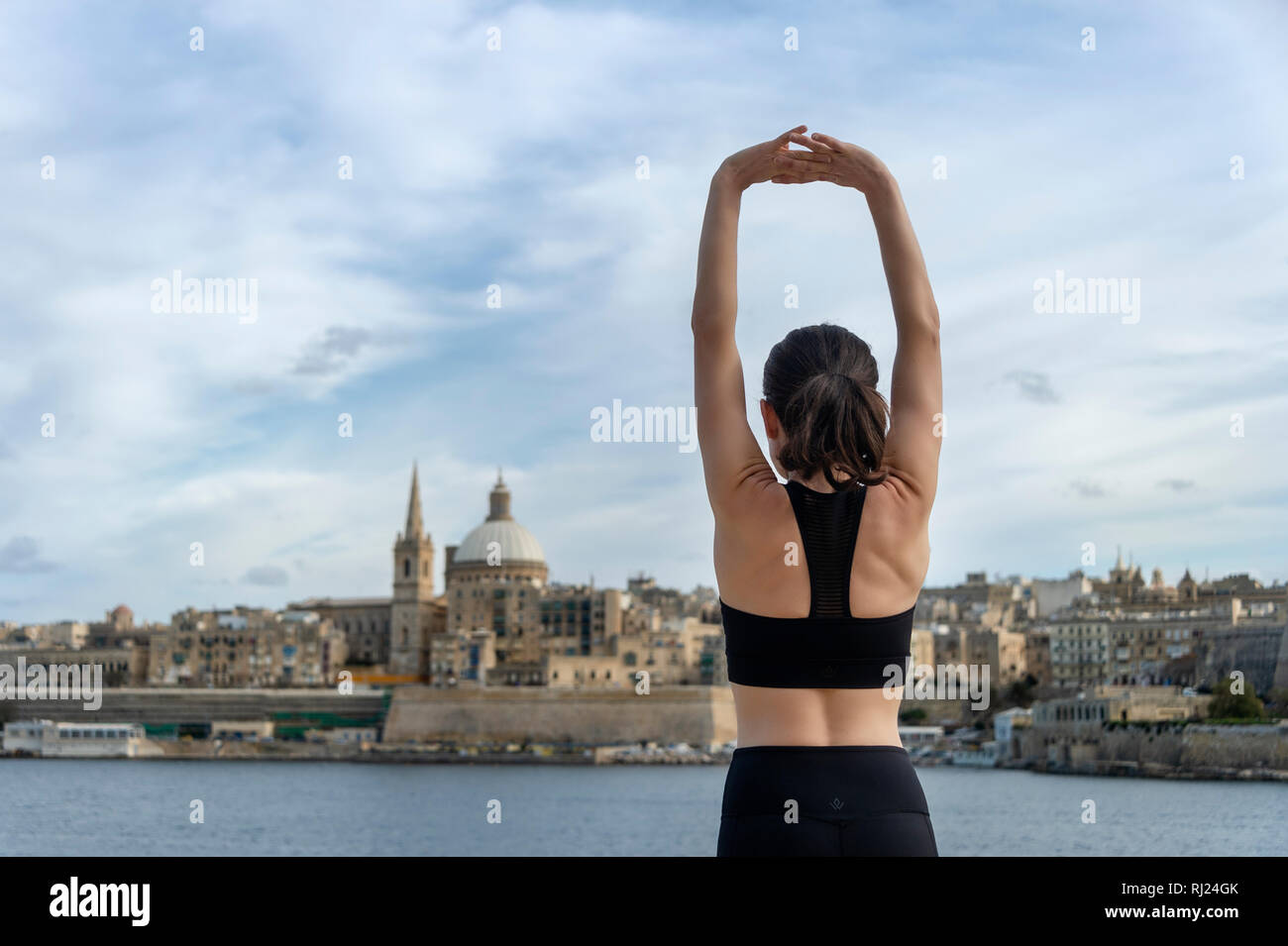 Vue arrière d'une femme faisant un bras extensible réchauffer l'exercice. La Valette Malte arrière-plan. Banque D'Images