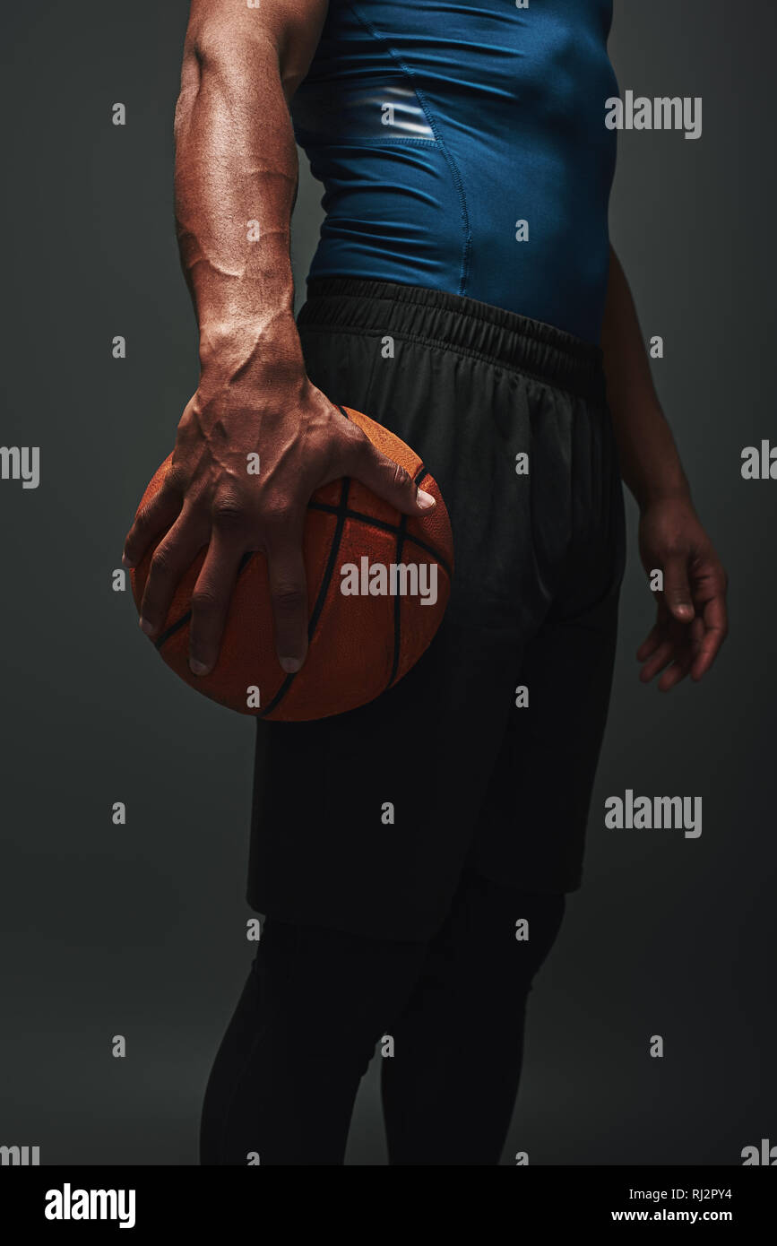 Close up of basket-ball en tee-shirt bleu et un short noir isolés sur fond sombre et tenant une balle Banque D'Images