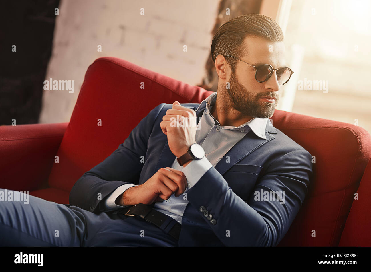 Les jeunes et le succès...d'affaires est assis sur un canapé dans un bureau moderne et à la recherche à travers des lunettes de soleil. Fashion look. Style d'affaires. Banque D'Images