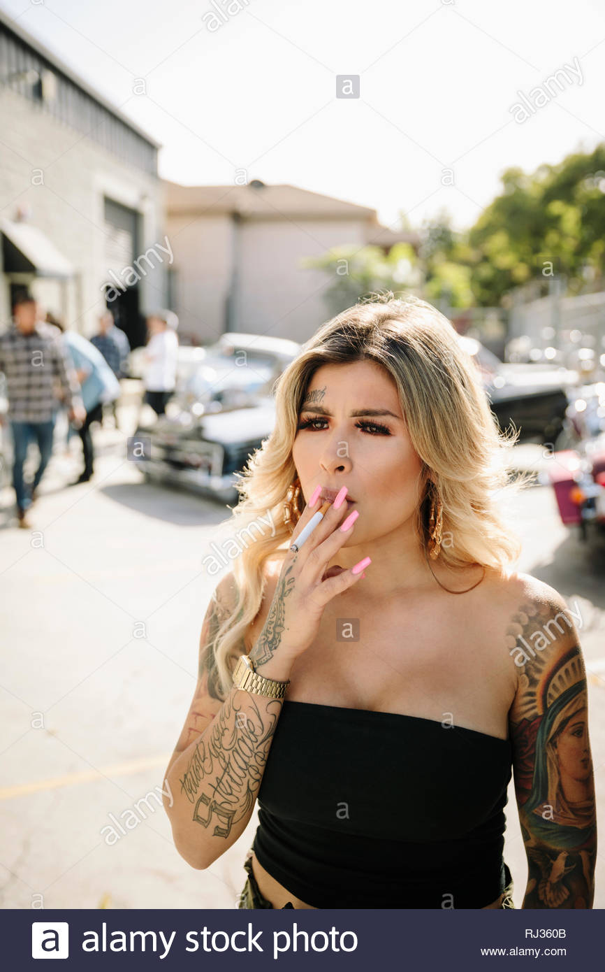 Jeune femme Latinx difficiles avec des tatouages cigarette dans parking ensoleillé Banque D'Images