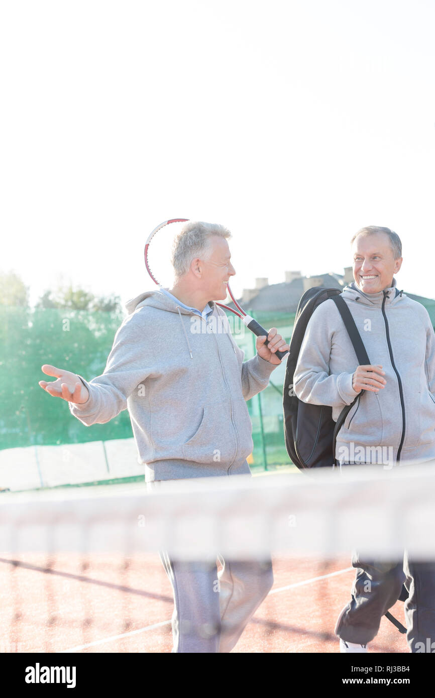 Smiling men dans les vêtements de sport à parler tout en marchant sur un court de tennis contre ciel clair Banque D'Images