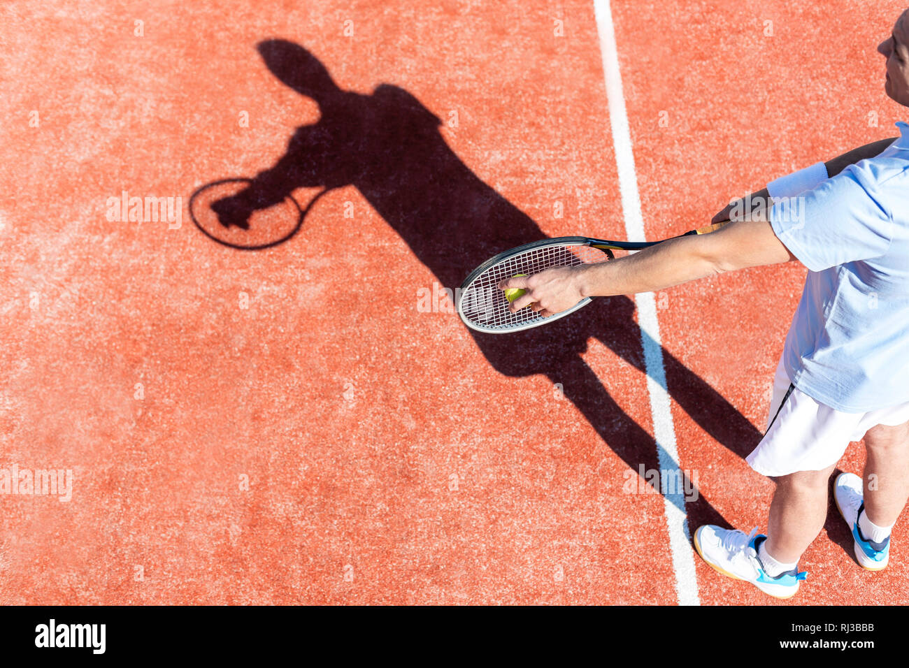 High angle view of mature man servant balle de tennis sur cour rouge Banque D'Images