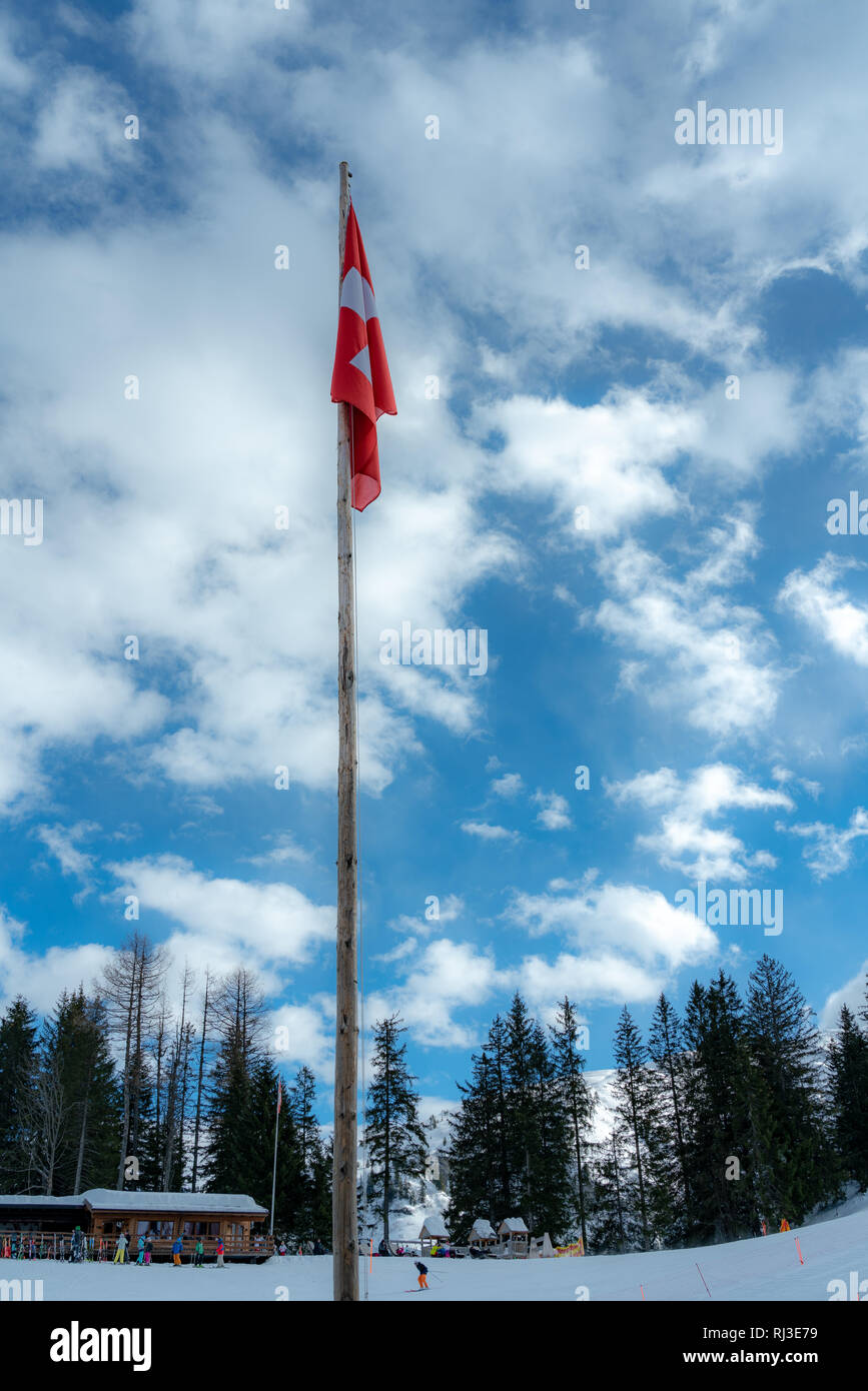 Le drapeau suisse pend mollement dans l'air hiver calme sur un mât en bois ancien, de nouveau ciel bleu avec des nuages blancs. Banque D'Images