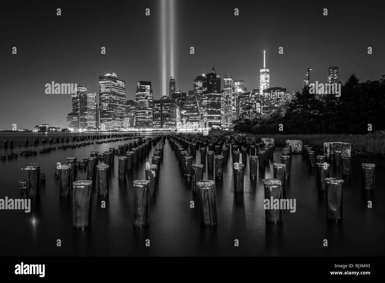 Pier pieux et l'hommage rendu à la lumière sur l'horizon de Manhattan de nuit, vu du pont de Brooklyn Park, à Brooklyn, New York. Banque D'Images