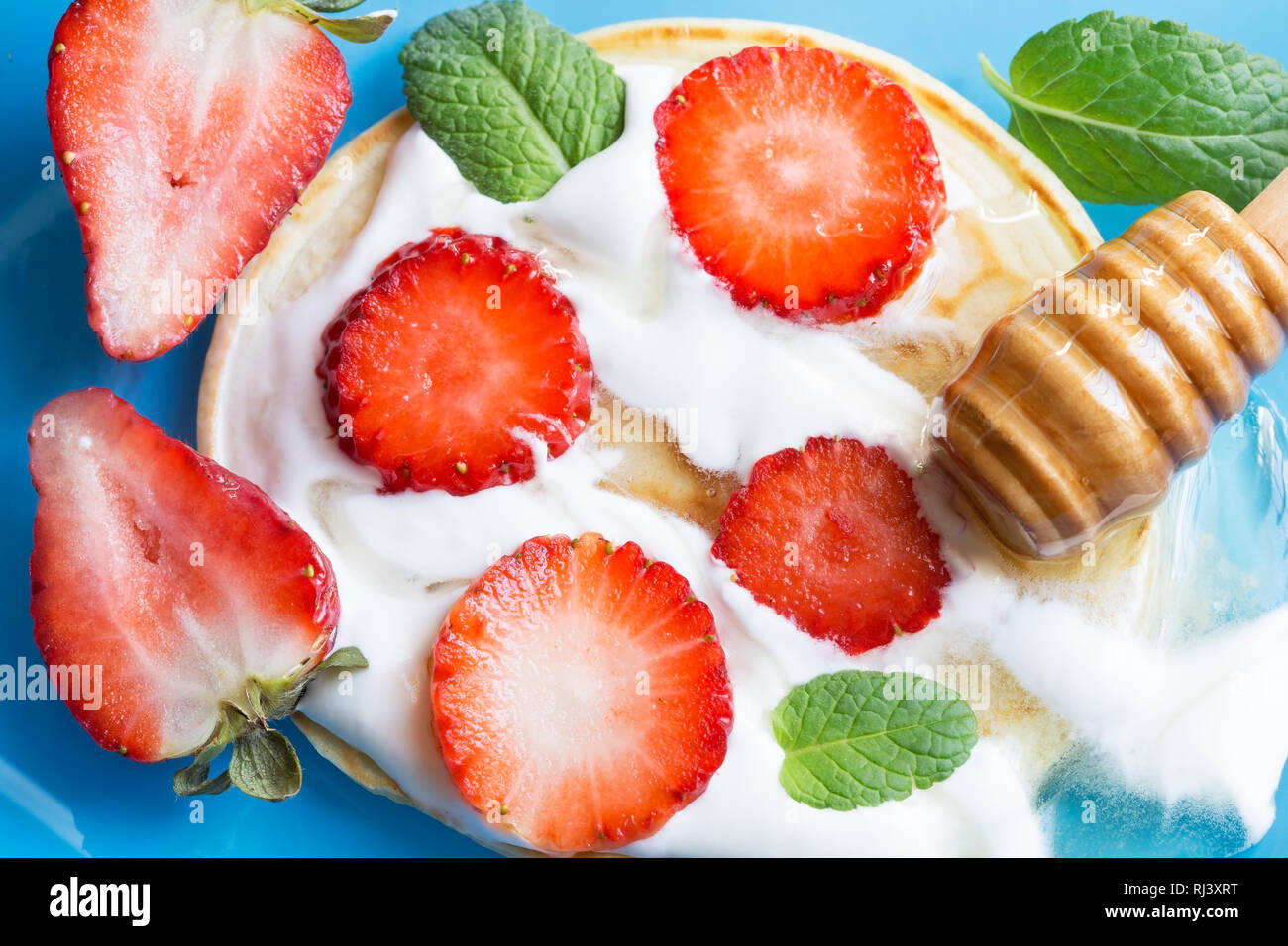 Crêpes aux fraises, miel et menthe sur une surface bleue Banque D'Images