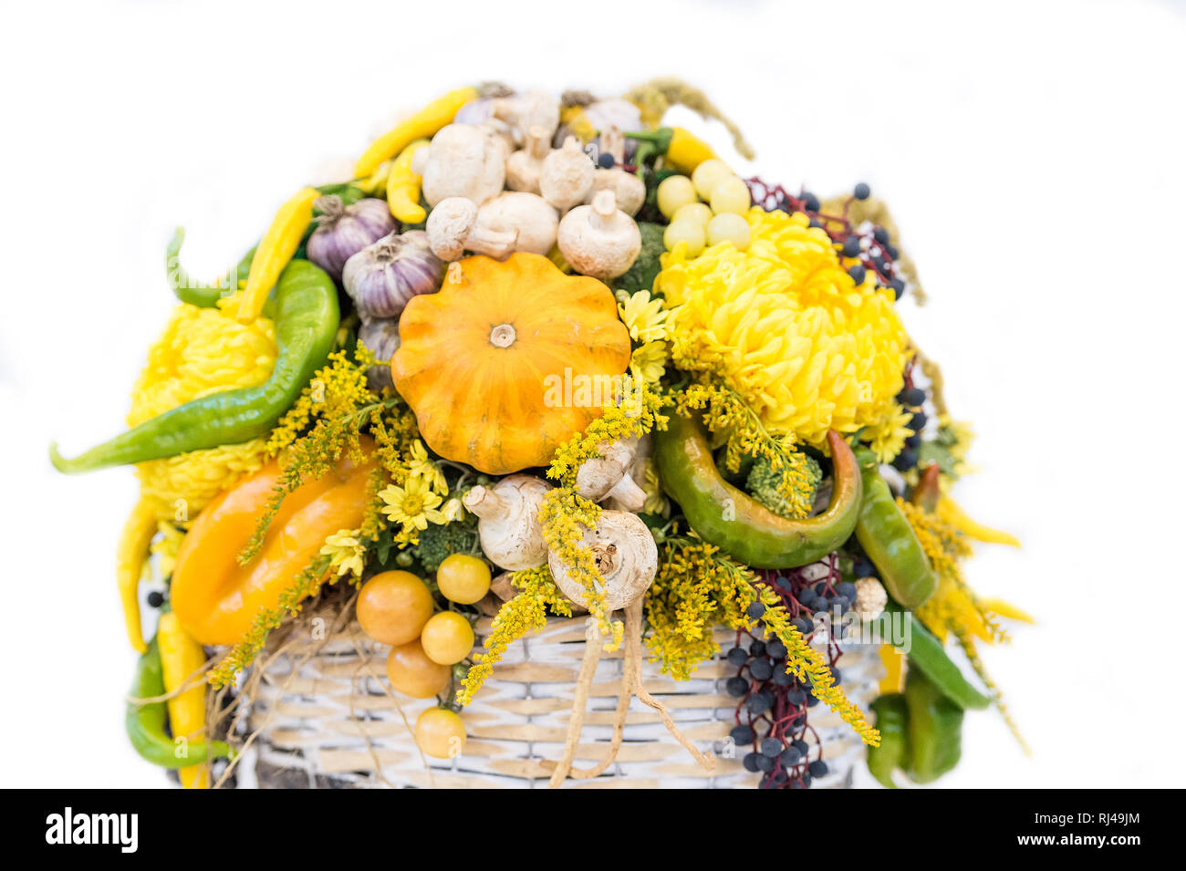 Composition florale décoration de légumes de saison ail poivre tomate champignons et raisins patison vert jaune et orange avec fleurs chrysanthème isolé sur blanc dans panier Banque D'Images