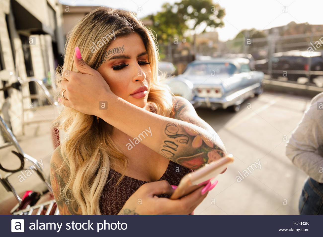 Jeune femme Latinx avec des tatouages à l'aide de smart phone sous le soleil de stationnement Banque D'Images
