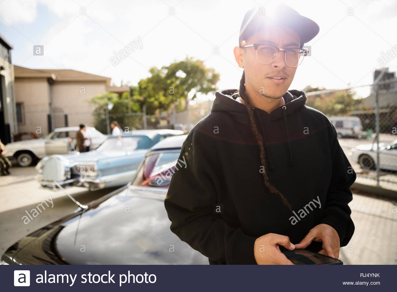 Confiant Latinx Portrait jeune homme avec une longue natte leaning on vintage car parking sous le soleil Banque D'Images