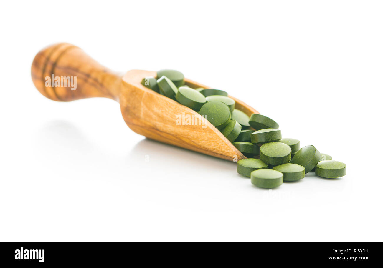 La chlorelle vert comprimés ou l'orge en pillsin scoop en bois isolé sur fond blanc. Banque D'Images