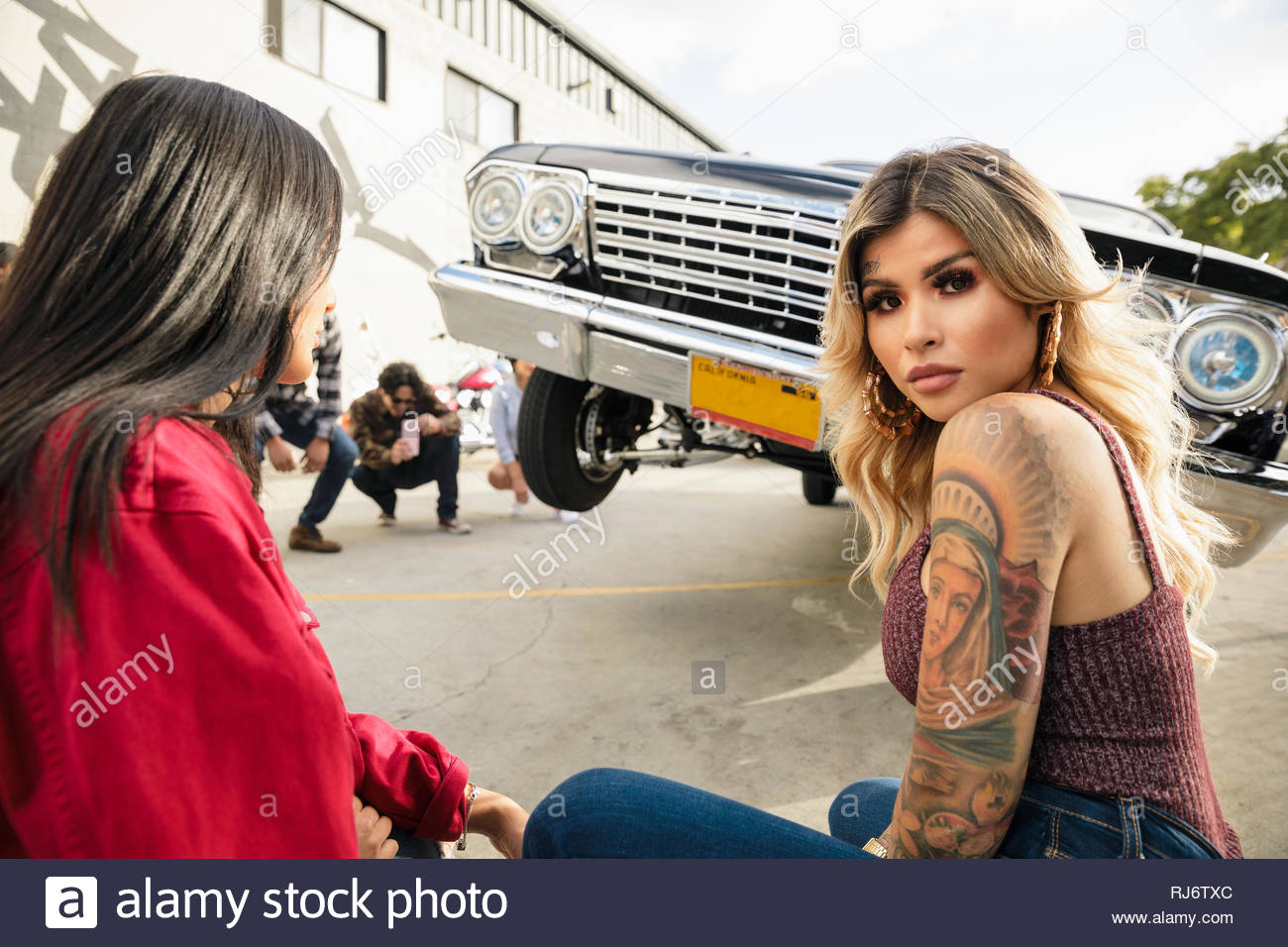 Confiant Latinx Portrait jeune femme avec des tatouages en face de low rider voiture stationnement en rebondissant Banque D'Images