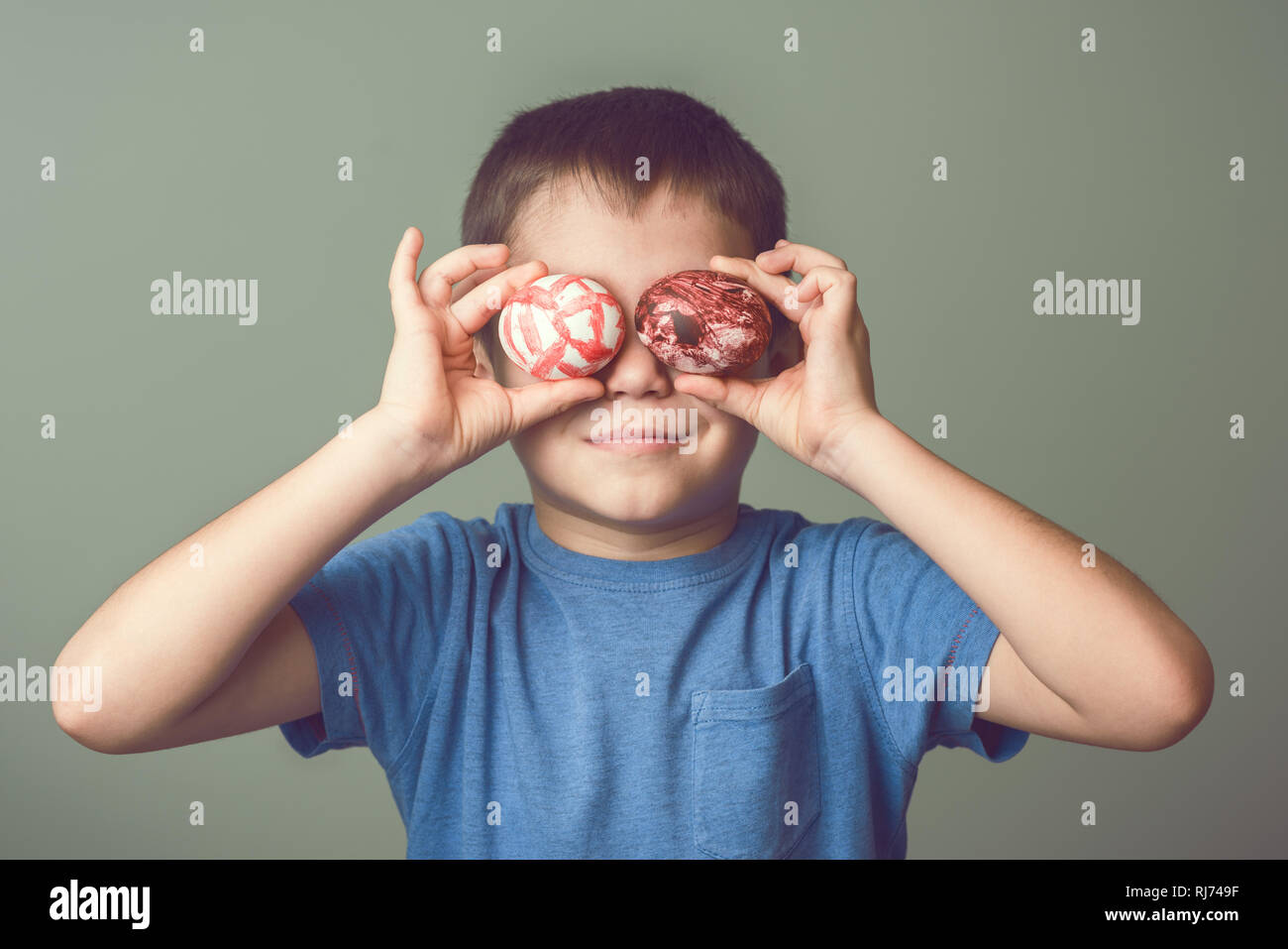 Un enfant est titulaire d'oeufs de Pâques peints à la main près de ses yeux. Fond vert. Idées de Pâques. L'espace pour le texte. Joyeuses Pâques. La tonalité de l'image. Banque D'Images