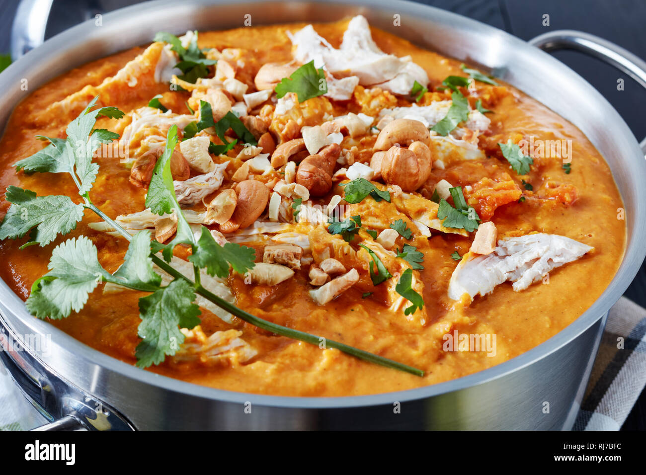 Close-up de soupe Mulligatawny épicé copieux avec de la viande de poulet frit arrosé avec dans un chaudron de cajou sur une table en bois noir, Indien et anglais c Banque D'Images