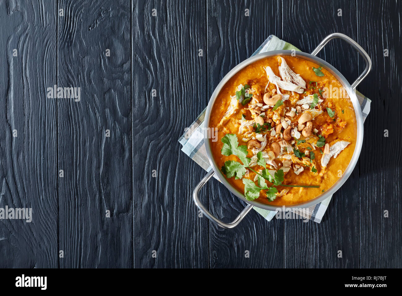 Soupe Mulligatawny épicé chaleureux avec la viande de poulet et le lait de coco saupoudré de cajou frits dans un chaudron sur une table en bois noir, Indien et engl Banque D'Images