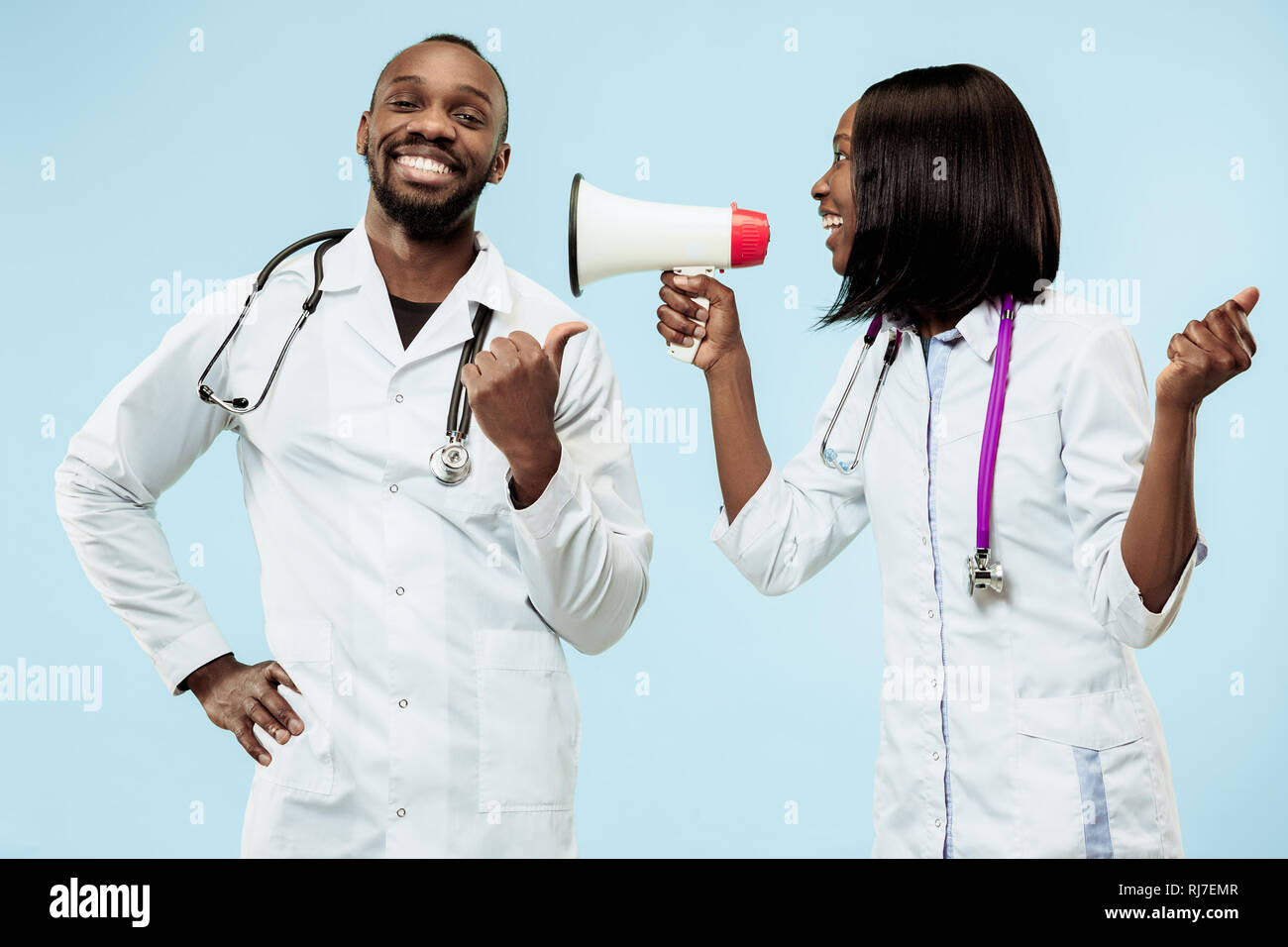 La femelle et mâle smiling happy afro-américain les médecins sur fond bleu au studio avec mégaphone. La clinique, médical, infirmier, santé, santé, hôpital, soins de santé, l'emploi, concept professionnel Banque D'Images