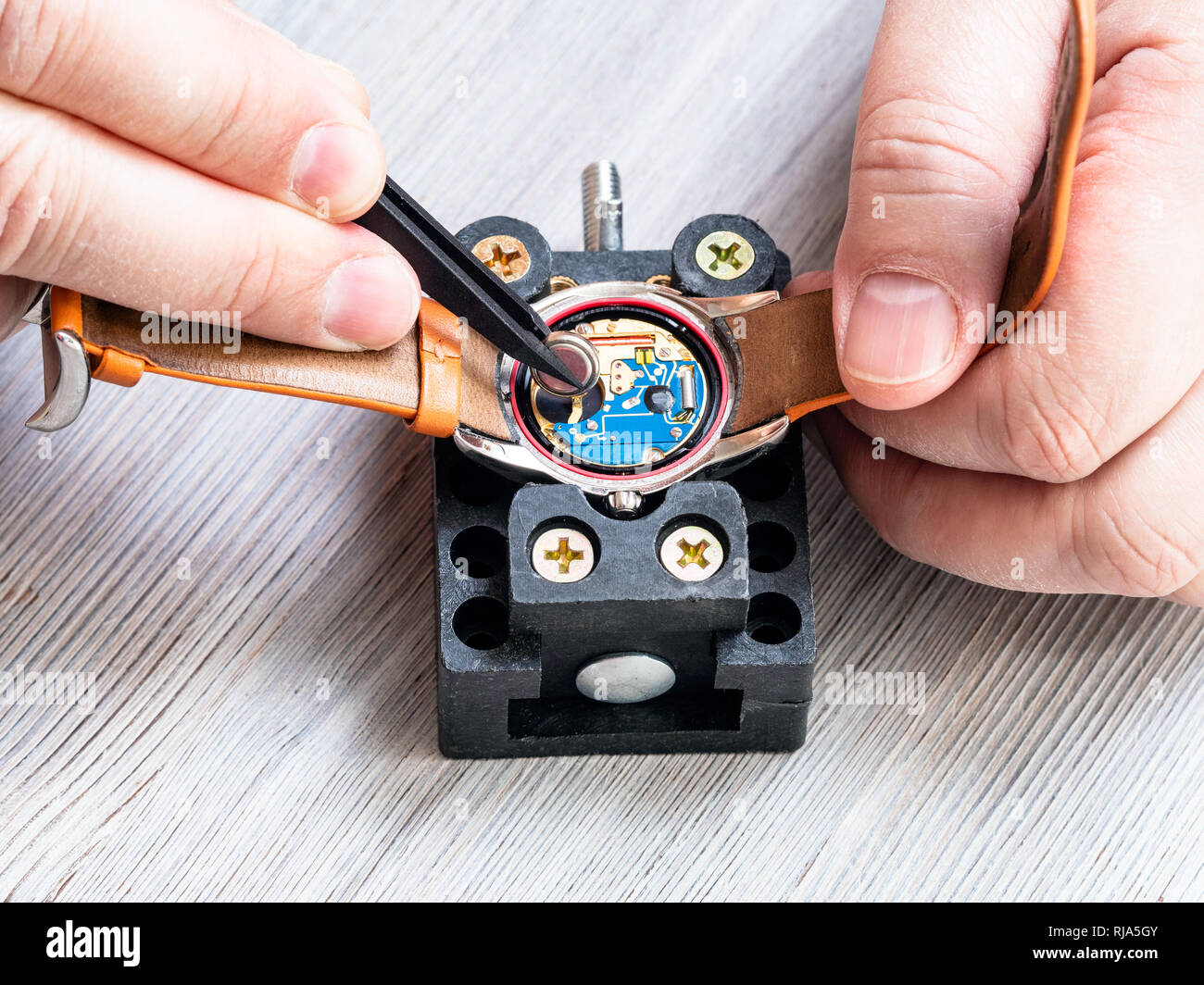 Atelier de réparateur watch - vue avant d'horloger du remplacement de la batterie dans la montre-bracelet à quartz avec des pinces en plastique sur la table en bois close up Banque D'Images