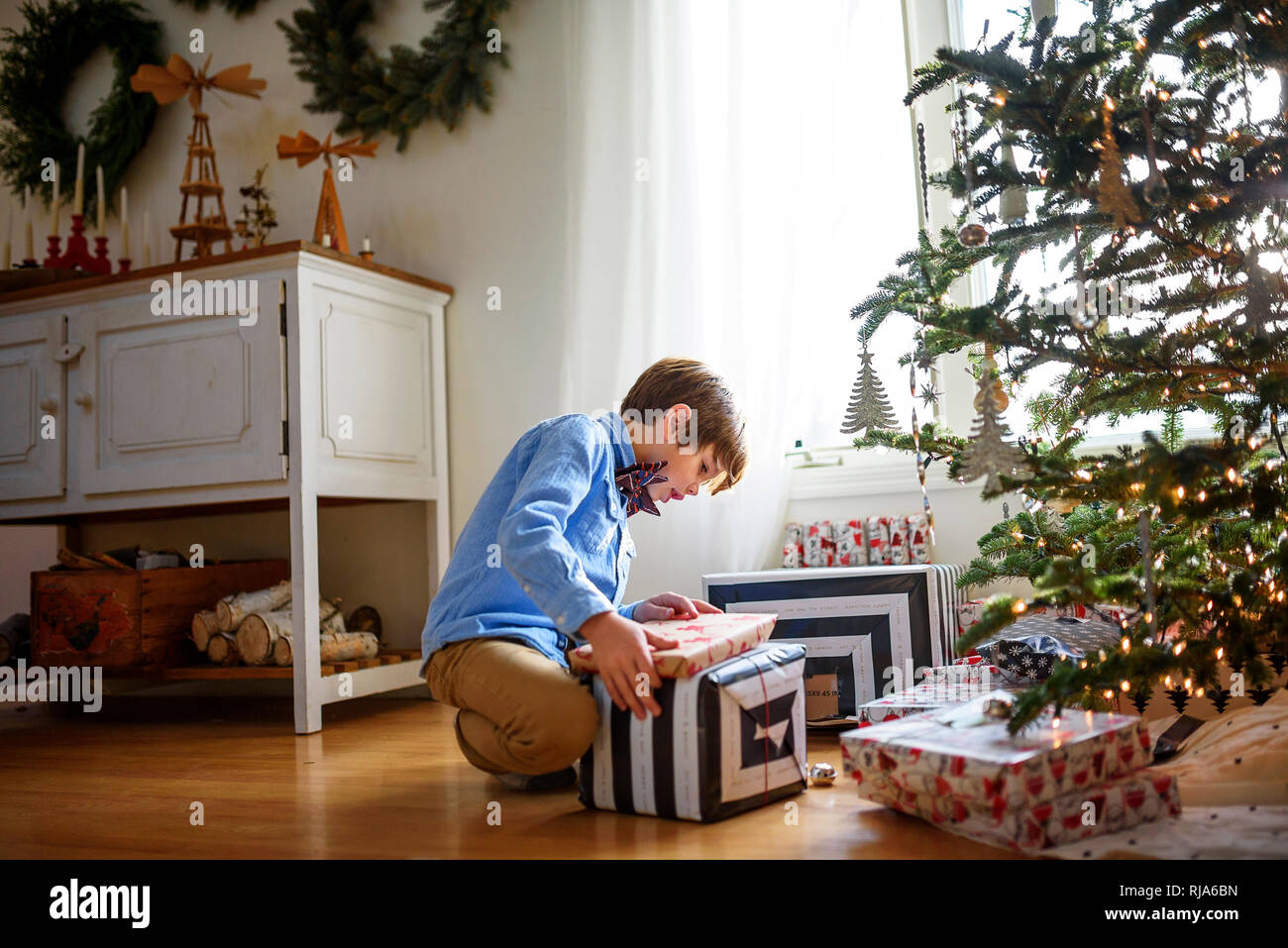 Garçon agenouillé devant un arbre de Noël à la recherche de cadeaux à Banque D'Images