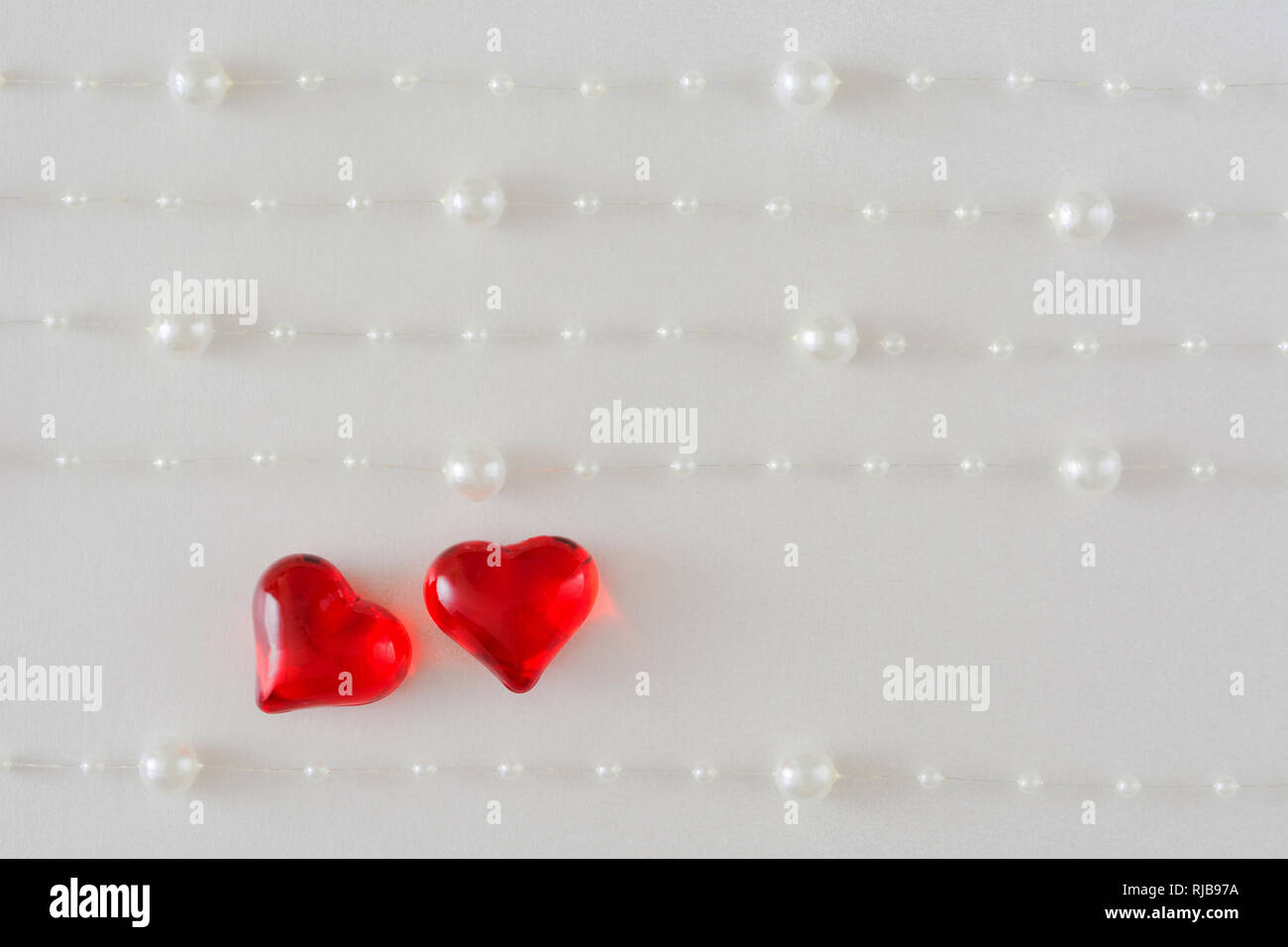 Fond de carte de mariage, la Saint Valentin avec deux coeurs brillants sur un fond blanc avec cinq cordes de perles blanches Banque D'Images