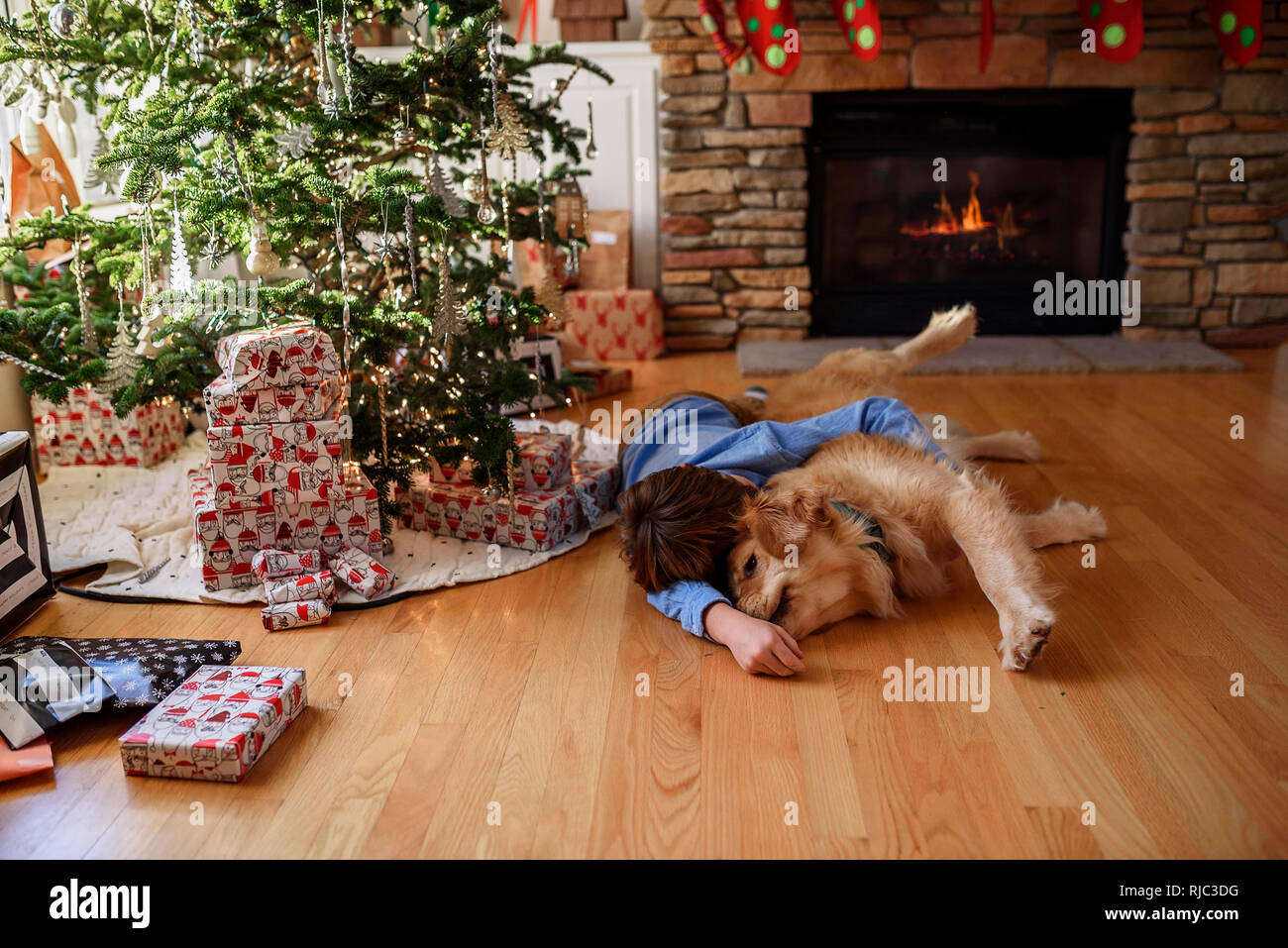 Garçon couché sur le sol en face d'un arbre de Noël de câliner son chien Banque D'Images