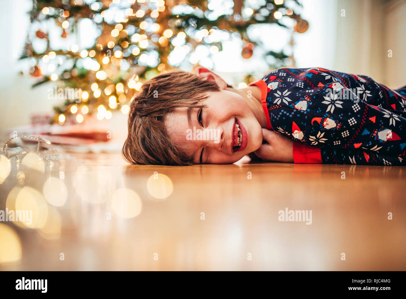 Garçon couché sur le sol en face d'un arbre de Noël de rire Banque D'Images