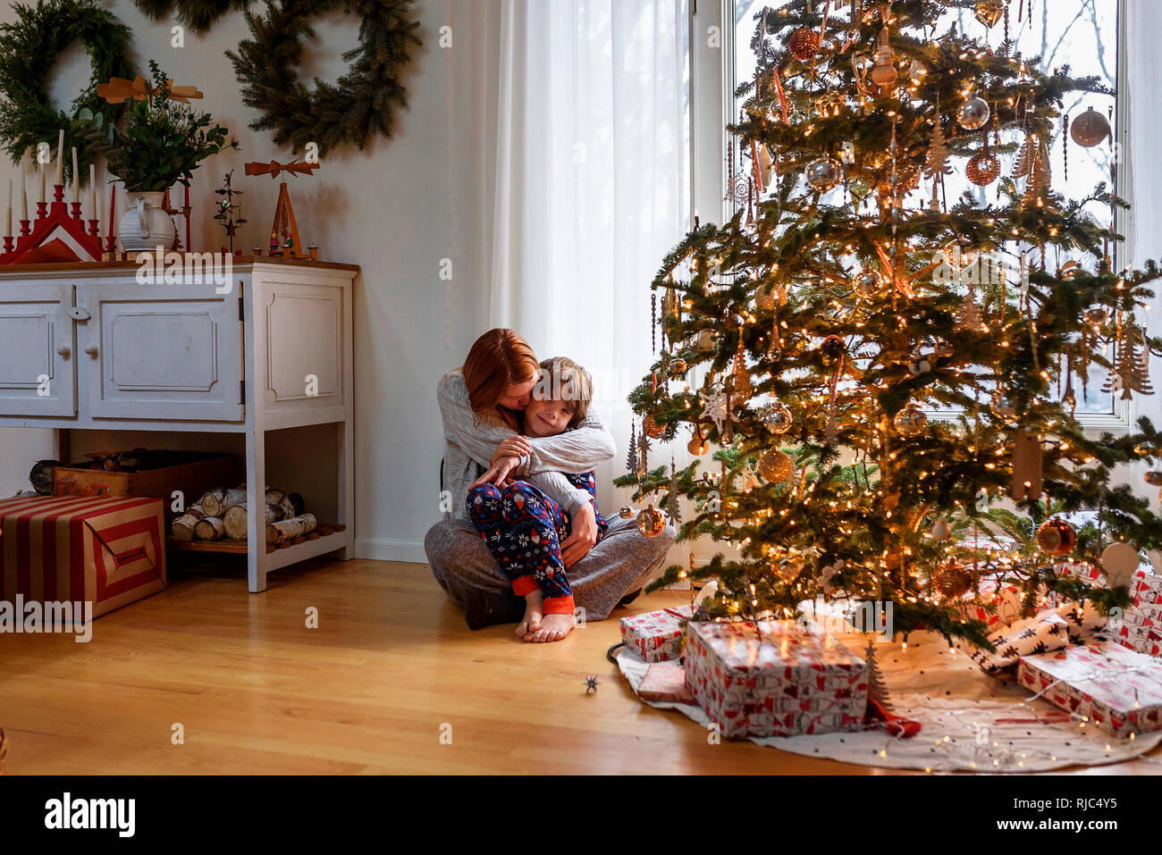 Woman sitting by a Christmas Tree hugging son fils Banque D'Images