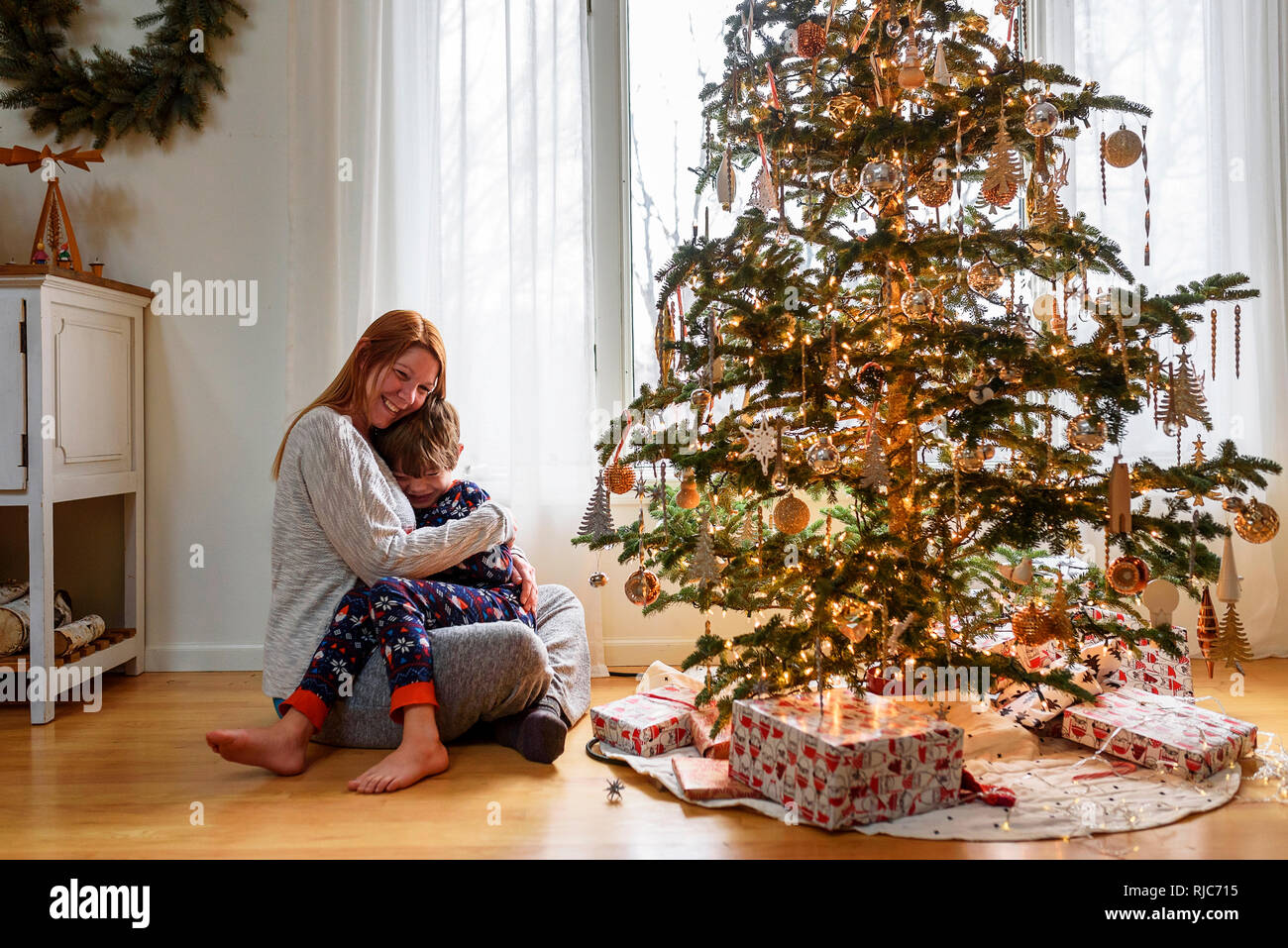 Woman sitting by a Christmas Tree hugging son fils Banque D'Images