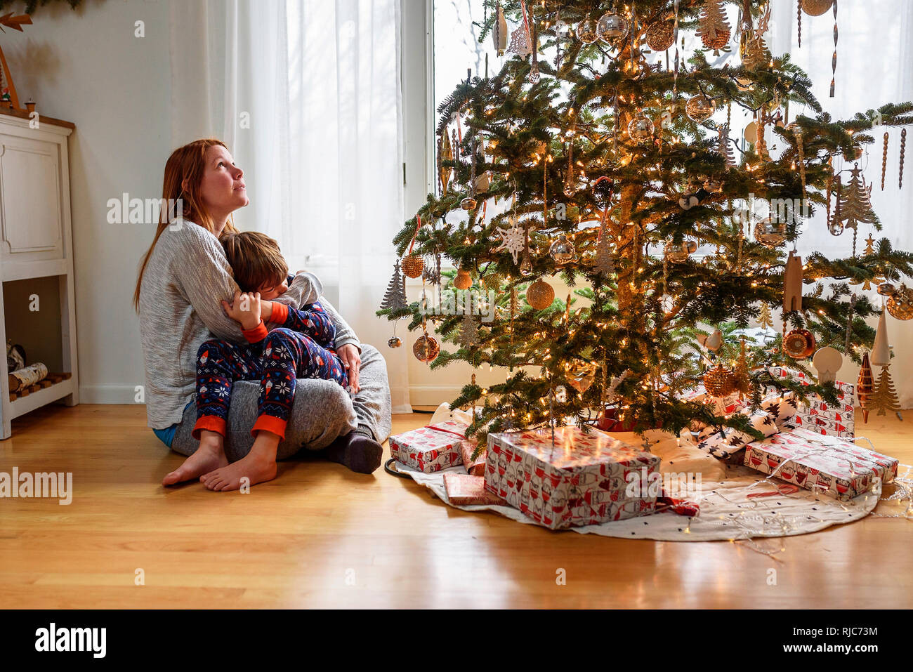 Woman sitting by a Christmas Tree hugging son fils Banque D'Images