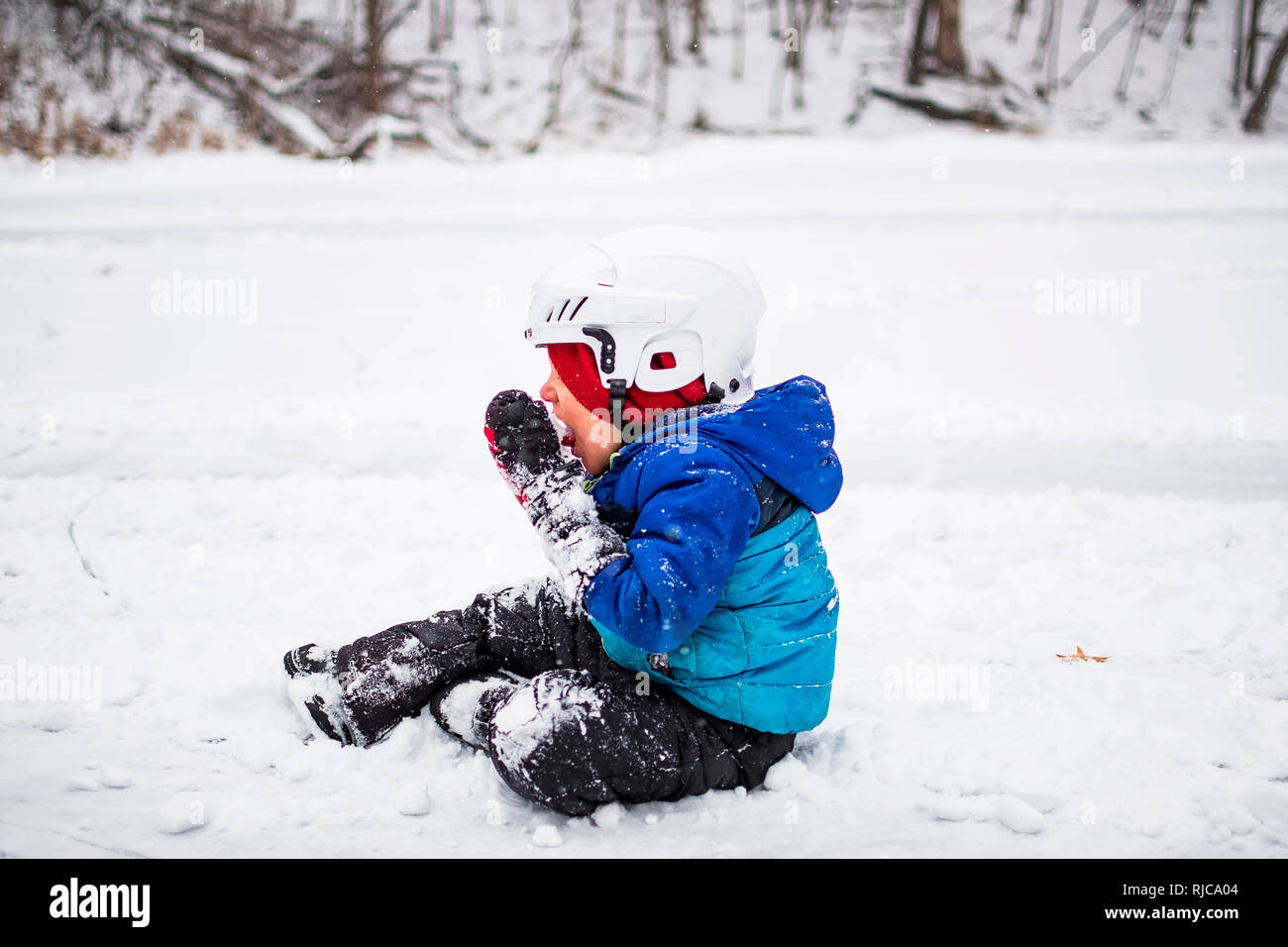 Garçon assis sur un lac gelé de manger la neige, Wisconsin, United States Banque D'Images