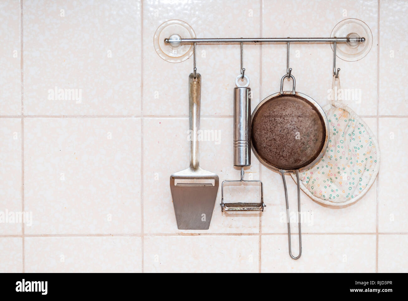 Des ustensiles de cuisine accroché au mur avec tamis, metal peeler et serviette monté avec ventouses gros plan du mur carrelé Banque D'Images