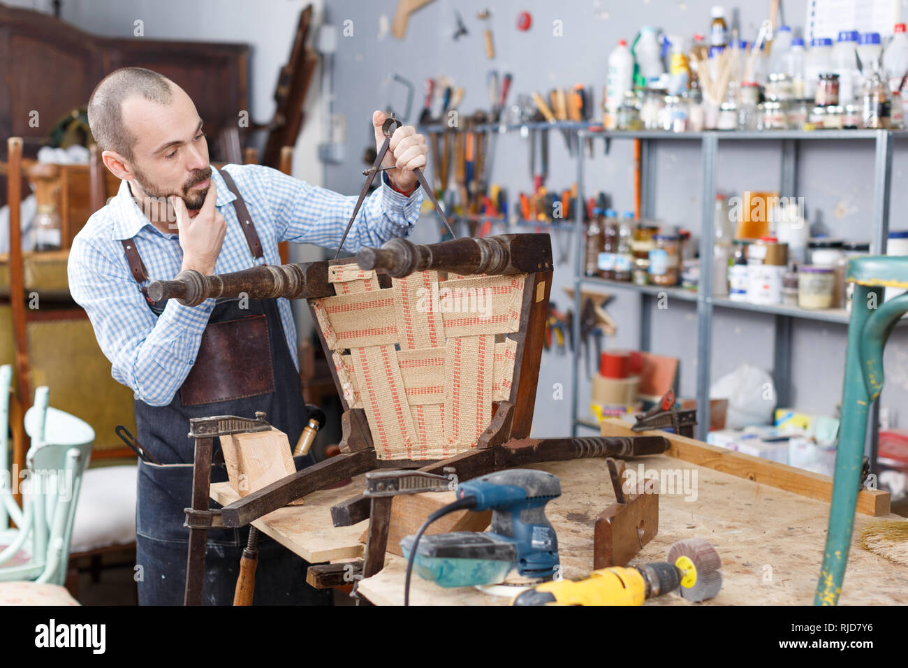 Jeune restaurateur à l'aide d'outils de mesure pour trouver des proportions de vieille chaise en bois studio Banque D'Images