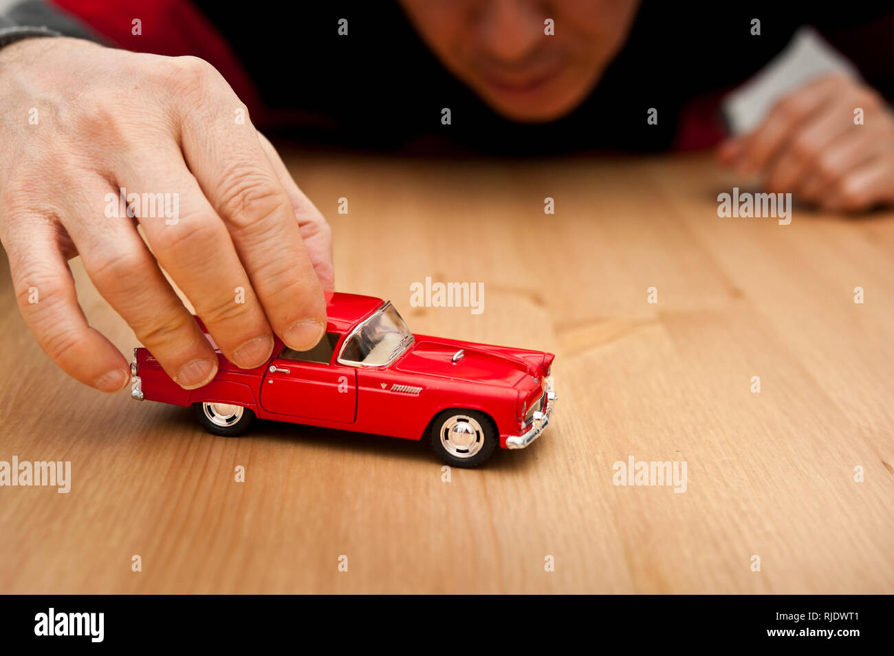 Homme adulte jouant avec un modèle de voiture Ford Thunderbid rouge sur la table Banque D'Images