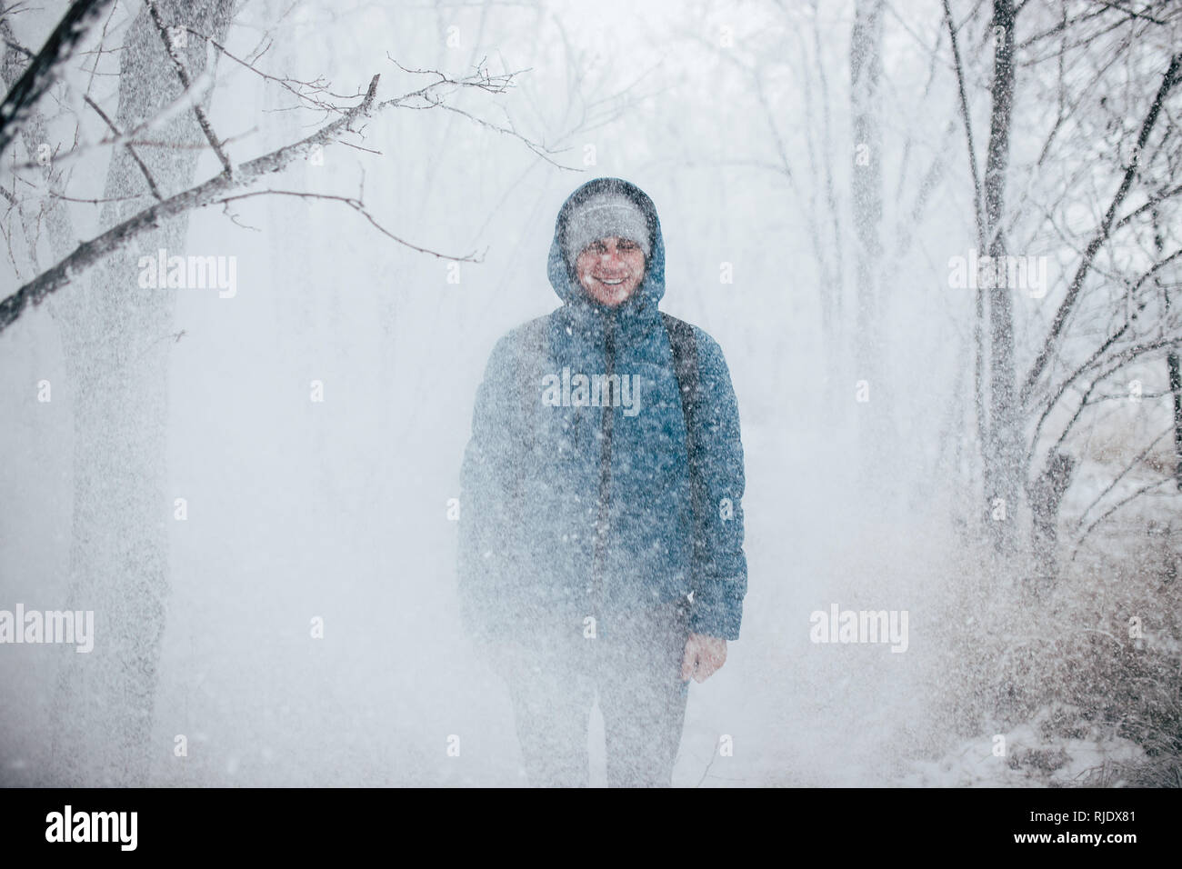 Un gars portant une chemise avec un capot est debout dans une forêt enneigée, la neige tombe sur lui à partir de ci-dessus. Banque D'Images Un gars portant une chemise avec un capot est debout dans une forêt enneigée, la neige tombe sur lui à partir de ci-dessus. Banque D'Images