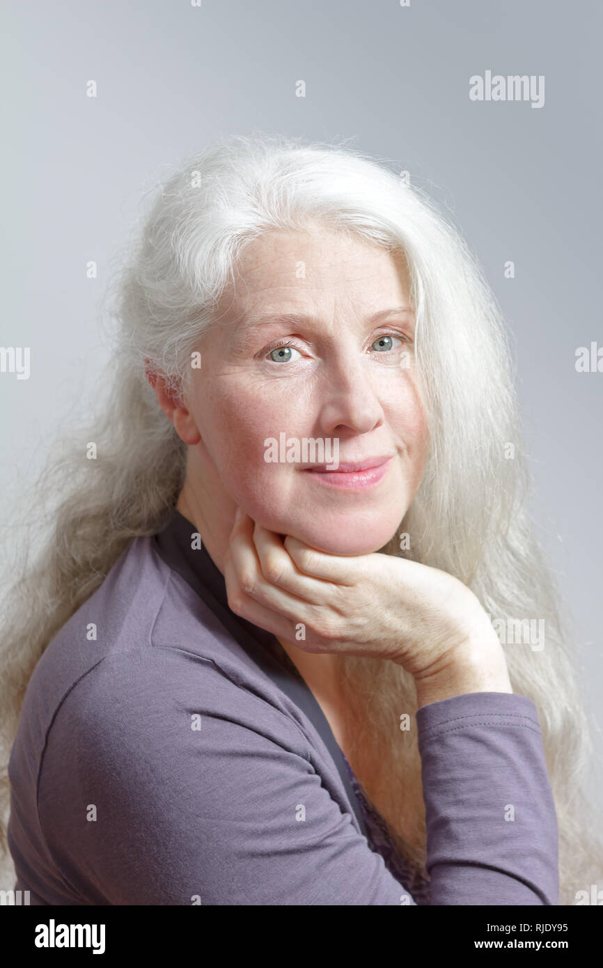 Portrait d'une jolie femme mature avec de beaux longs cheveux blancs devant un fond gris. Banque D'Images