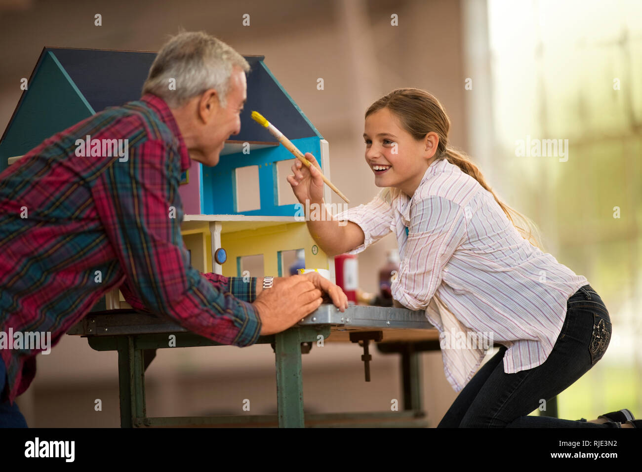 Happy girl et son grand-père s'amusant à peindre une maison de poupées à l'intérieur d'un garage. Banque D'Images