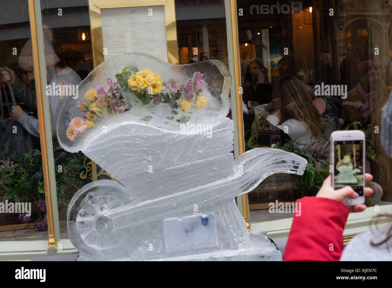 Personne prenant une photo avec son téléphone d'une sculpture sur glace de brouette avec des fleurs congelées, York Ice Trail, Stonegate, York, North Yorkshire, ROYAUME-UNI. Banque D'Images