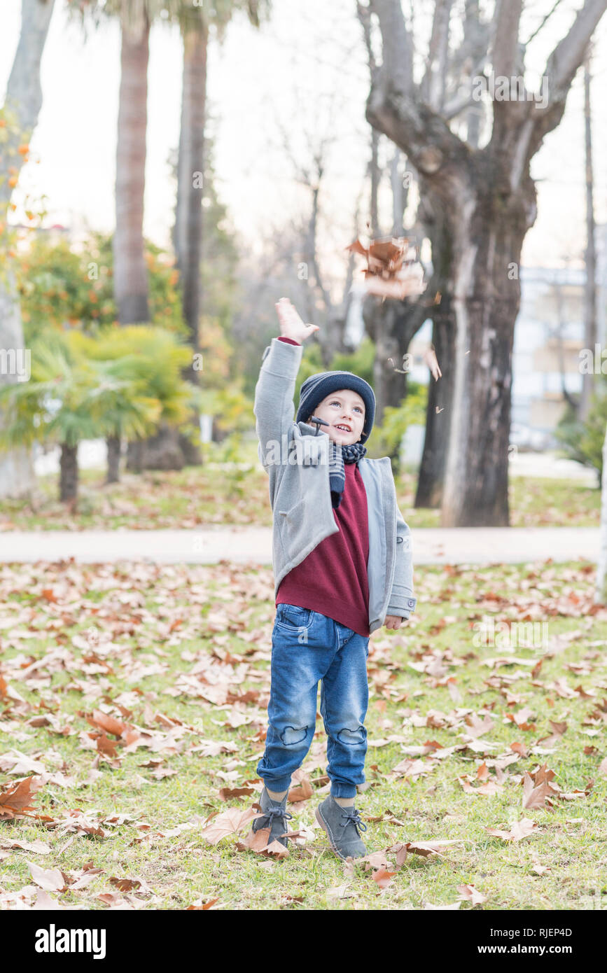 Enfant habillé en vêtements chauds Jeter feuilles mortes dans l'air Banque D'Images