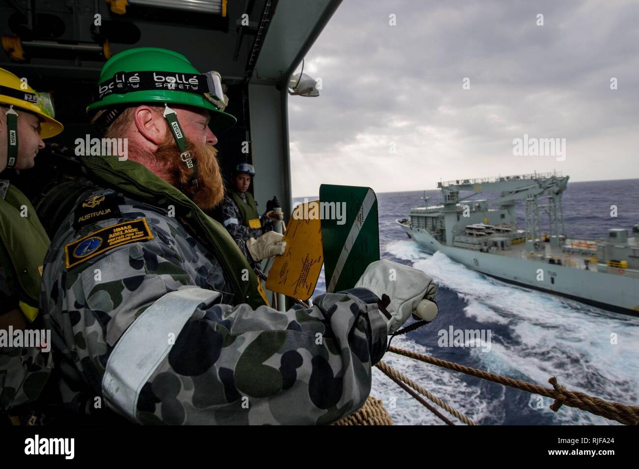 En mer (19 juillet 2018) de la Royal Australian Navy Matelot maître de Manœuvre Zackary Kelly, de Sydney, les signaux de l'hélicoptère du navire de débarquement quai HMAS Adelaide (L01) de la Marine royale du navire MV Astérix lors d'un ravitaillement en mer au cours de Rim of the Pacific (RIMPAC), le 19 juillet. Vingt-cinq nations, 46 navires, 5 sous-marins, et d'environ 200 avions et 25 000 personnes participent à l'EXERCICE RIMPAC du 27 juin au 2 août dans et autour des îles Hawaï et la Californie du Sud. Le plus grand exercice maritime international RIMPAC, fournit un ensemble unique de trai Banque D'Images