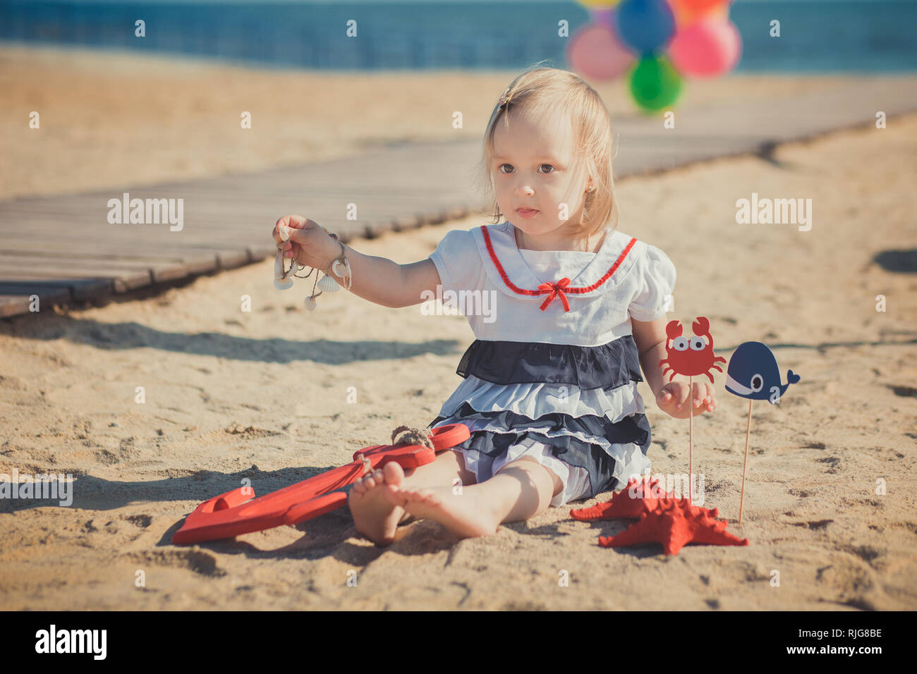 Bébé Enfant fille Cute blonde posing bénéficiant de temps de la vie d'été  sur la plage de sable de la mer sur la jetée en bois colorés avec beaucoup  de ballons portant