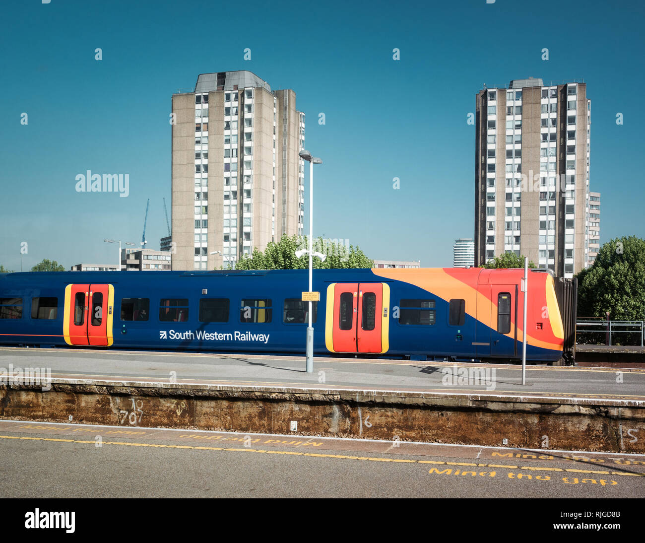 London, Royaume-Uni - Mai 19, 2018 : South Western Railway train locomotive sur la plate-forme en attente pour les voyageurs avec deux gros immeuble d'appartements dans l'arrière-plan Banque D'Images