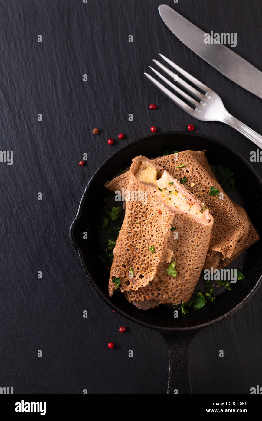 Concept alimentaire jambon et fromage fait maison en crêpe poêle de fer moulé sur fond d'ardoise noire Banque D'Images