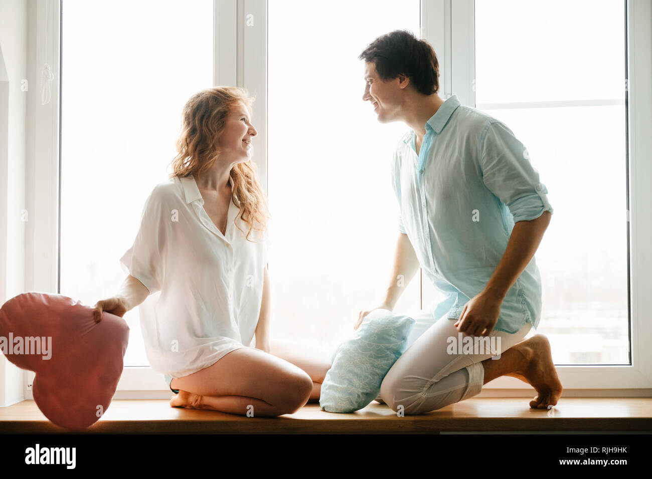 Fille Couple et guy jouer avec des oreillers près de fenêtre. Banque D'Images