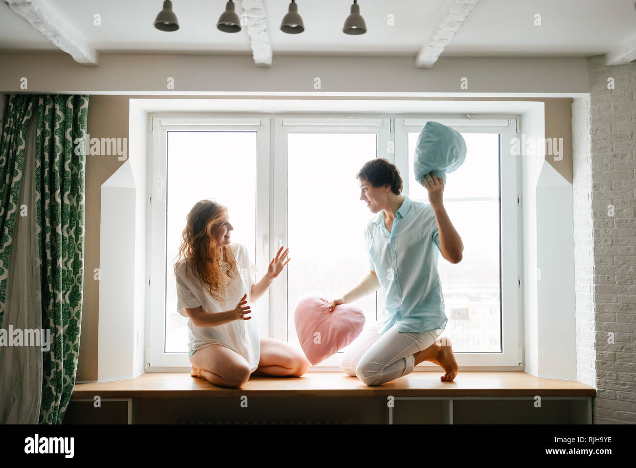 Fille Couple et guy jouer avec des oreillers près de fenêtre. Banque D'Images