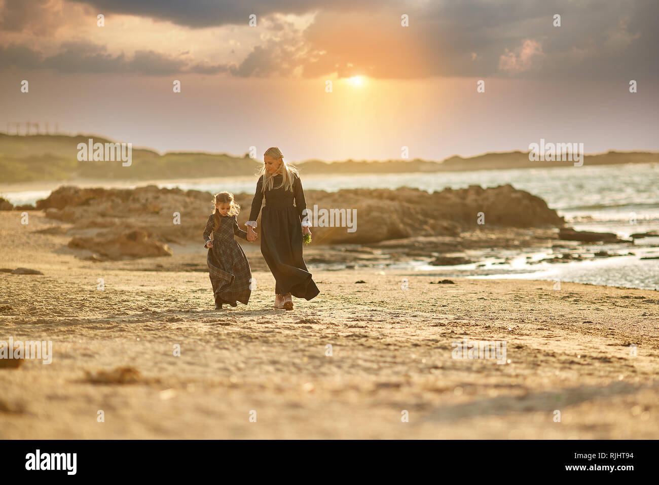 Femme et fille de longues robes retro marche sur la mer de sable au cours incroyable coucher du soleil Banque D'Images