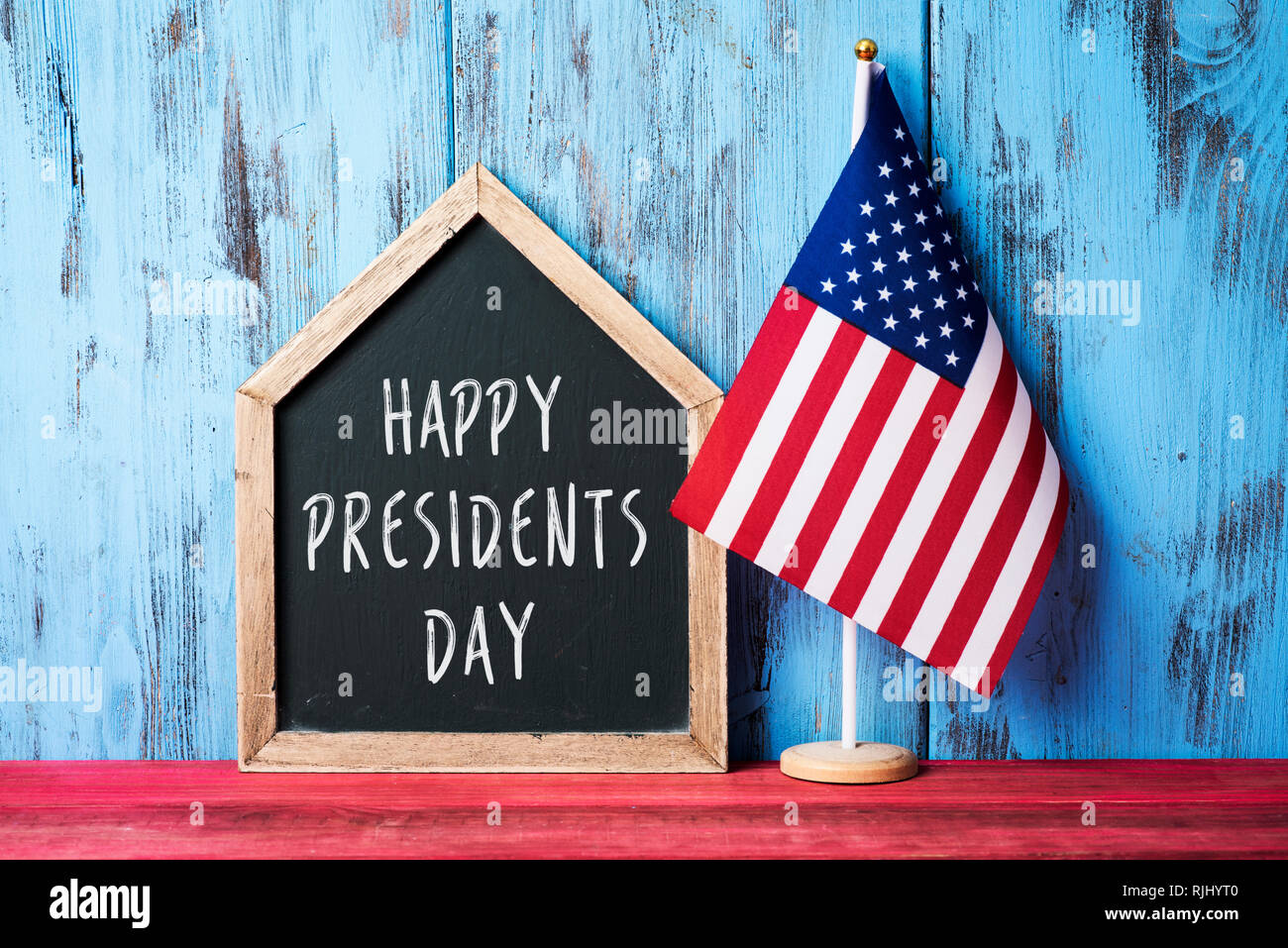 Un drapeau américain et une maison en forme de tableau avec les présidents du texte écrit en journée sur une surface en bois rouge, against a blue background Banque D'Images